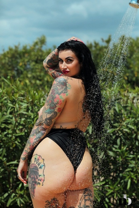 Chubby and Cherrie Pie, who has tattooed hands and a beard, pose in the swimsuit outdoors while showering.