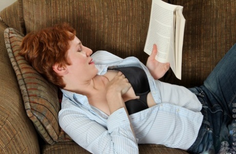 Short, ginger Gigi strips and masturbates while reading a book.