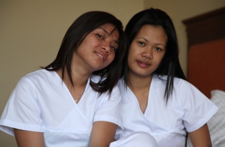 A group of sexy Filipino nurses, Joanna and Joy, pose for a picture on the bed in their white uniforms.