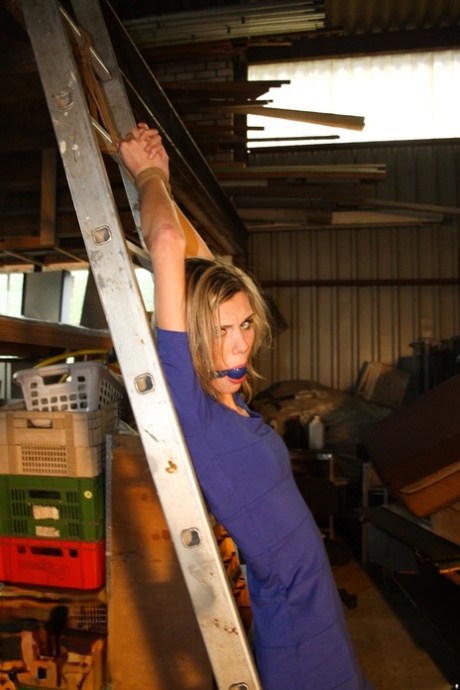 Amateur hairstylist Irena, who is blonde at the time, gagged and tied up to a ladder while fully clothed for a garage grope.