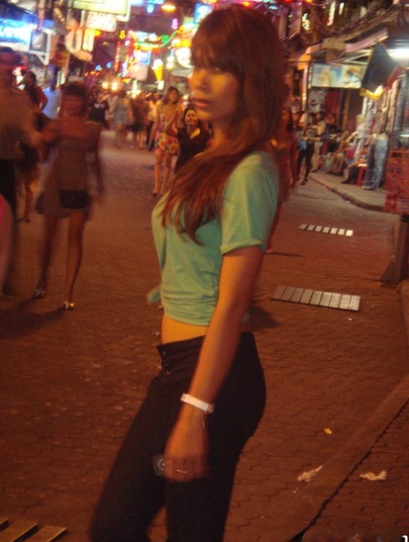 On the night streets, a tourist takes pictures of ladyboys while walking with them.