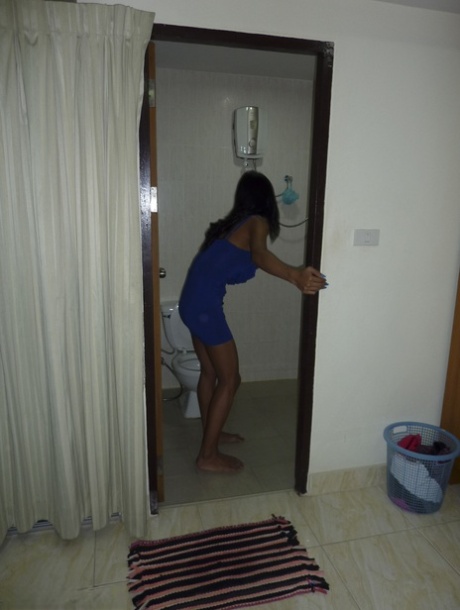 A blue-colored ladyboy with dark skin and hair flashes black panties in his dark brown dress in the bedroom.