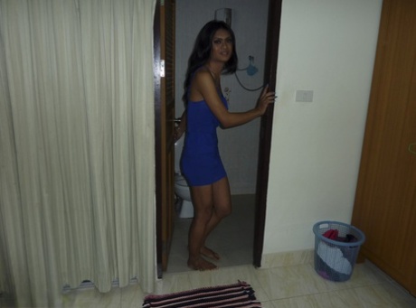 In the dark bedroom, a ladyboy with dark skin and blue clothing flashes black panties alone.