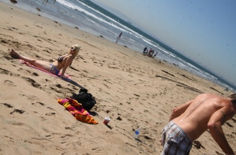 On the beach, slouchy blonde Siri displays her broad legs in a bikini while enjoying the sun.