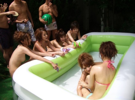 Japanese females in bikinis are seen taking pictures and playing in a small outdoor swimming pool.