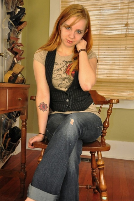 The teenager with tattooed redhead, Paige, teases and snatches herself while sitting on a chair.