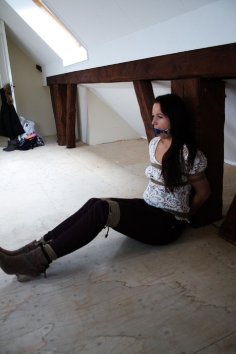 Ball-gagged brunette Lena posing with her hands tied to a wooden table.