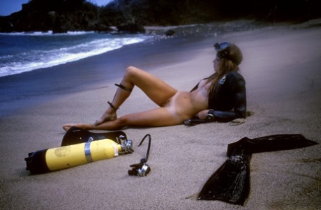 Barbie Lewis, a blonde, is nude on the beach while wearing her diving gear.