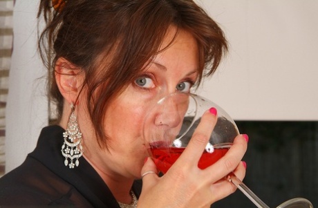 The lovely, adult woman Marishka strips and holds a large glass of wine in her mouth.