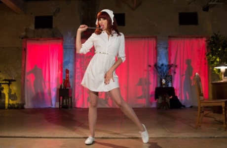 Redhead nurse Maitress Madeline Marlowe pulls off a seductive striptease on stage.