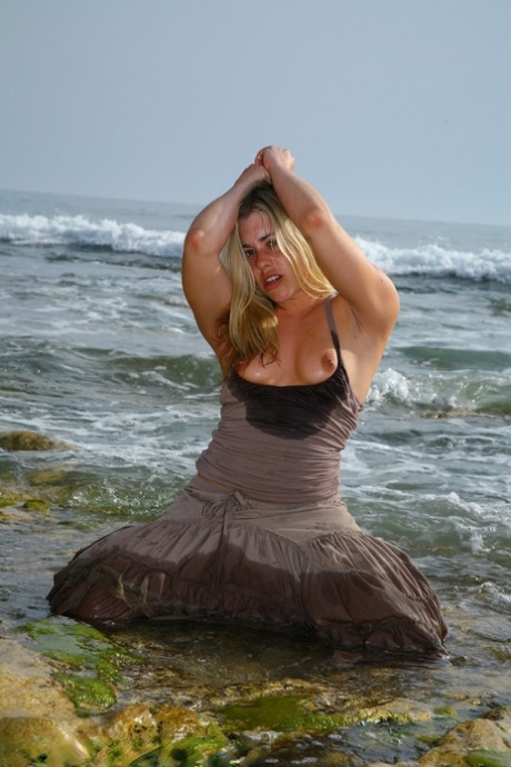 British model Tammy Oldham takes a masturbation pose and sedes on the sandy shoreline.