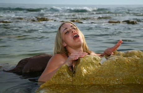 The British model Tammy Oldham engages in provocative self-pleasure while posing on a sandy beach.