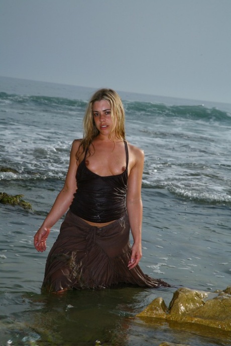 Tammy Oldham, a British model known for her seductive style, poses on a sandy beach and engages in self-pleasure.