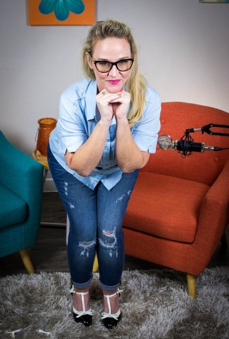 Displaying his flirty blonde glasses, Dee Siren wears a pair of attractive jeans and blue top.