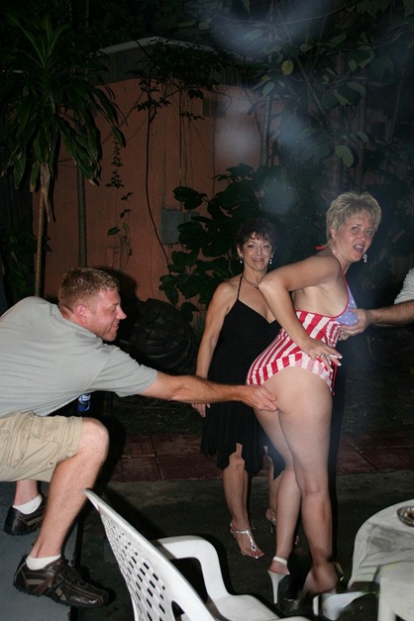 Adult, casual swinger partners engaging in playful teasing and French kissing at an event.