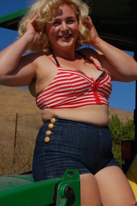 Poppy Cox's chubby blonde hair appears in the shape of curves and hair extensions as she strips off on a tractor.