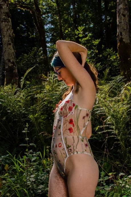 Underneath the forest, Minerva Fury exposes her hairy body in a tall and hippie-like attire, wearing eyeglasses.