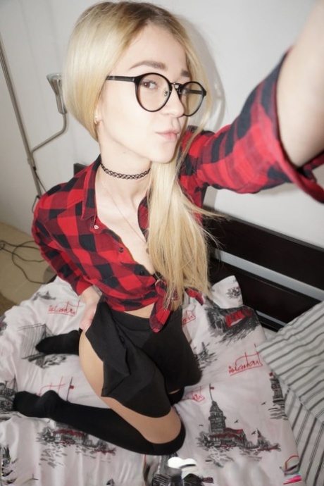 While wearing glasses, a young amateur with blonde hair sheds her attire and takes provocative selfies.