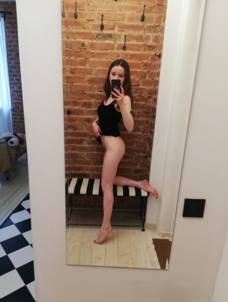 Sexy: A short brunette poses in front of a mirror, taking selfies while stripping and looking at herself in a sexy pose.