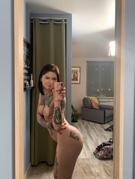 Posing in front of a mirror, the playful brunette displays her tattooed body as she enjoys her day.