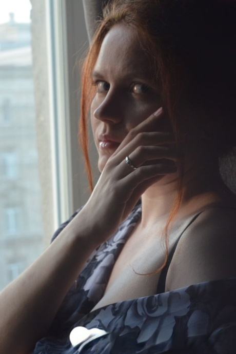 By the window, a redheaded model of amateur status stands and her large juicy breasts are touched.