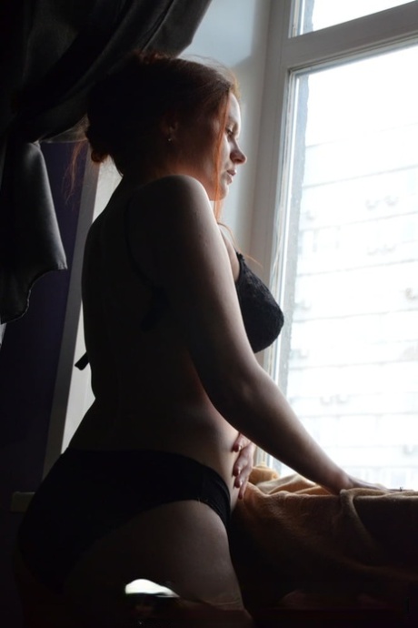 Near the window, a redheaded model of amateur standing stature puts her hands on her sizable juicy breasts.