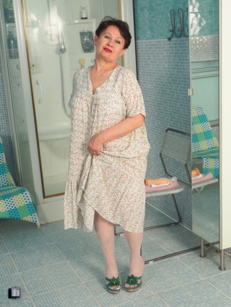 Granny Nata, who has short hair and is curly-haired, inserts a dildo into the bathroom mirror for her sexual experience.