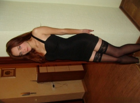 Slowly, the redheaded amateur removes her black dress and poses in stockings for a picture.