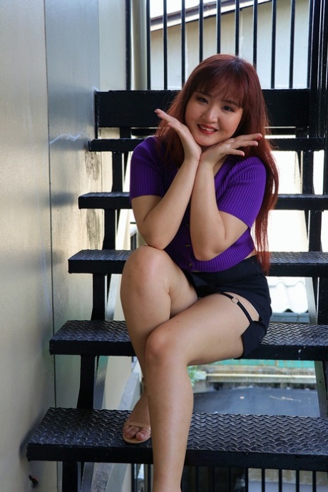 The redheaded Asian beauty is pictured on the stairs in her radiant skirt and purple top.