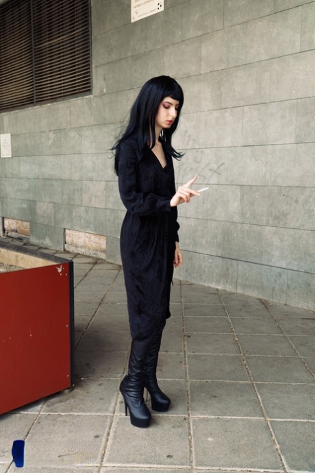 Raven-haired woman poses in her sexy black outfit and boots in public