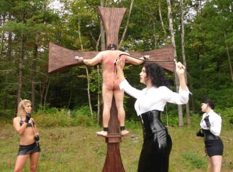 Three skinny dommes whip their sexually exploited slaves to an outdoor cross.